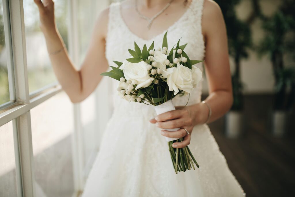 pexels-photo-30029366-30029366 Bride in a white dress holding a rose bouquet near a window, capturing elegance and romance.